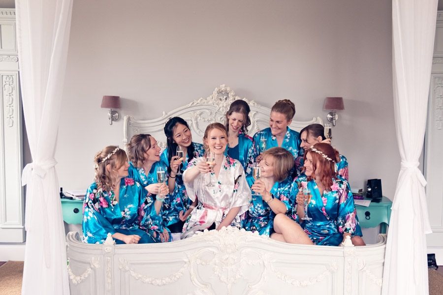 Bridesmaids in floral robes piled on to a four-poster bed with champagne
