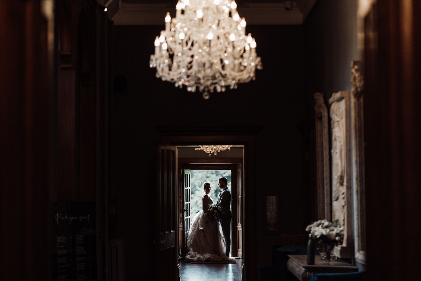 A couple in silhouette in the doorway at the end of the hall, the chandelier lit above