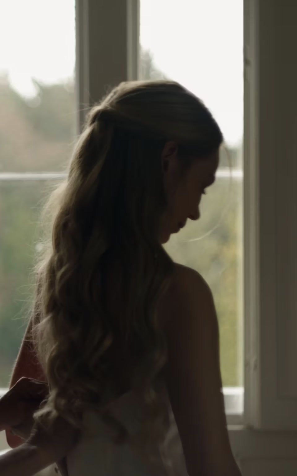 A bride by the window on the morning of her wedding, her face turned to the light