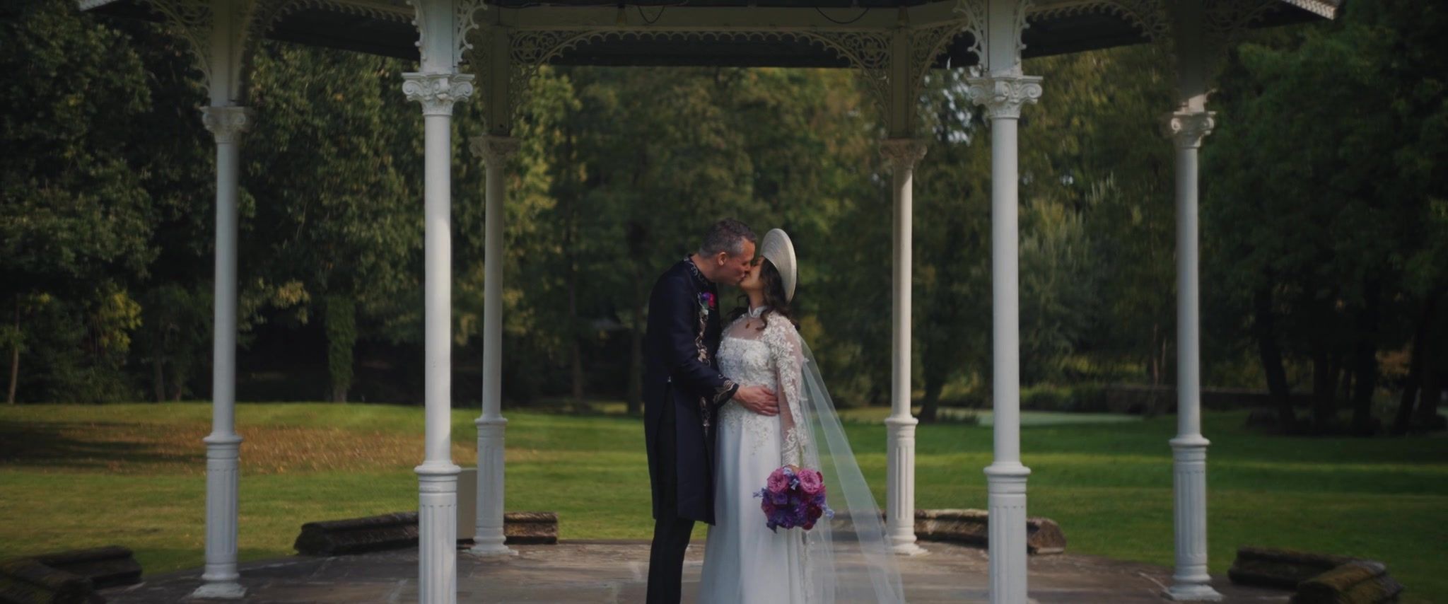 Dominique and Mike kiss beneath the white bandstand in the orchard